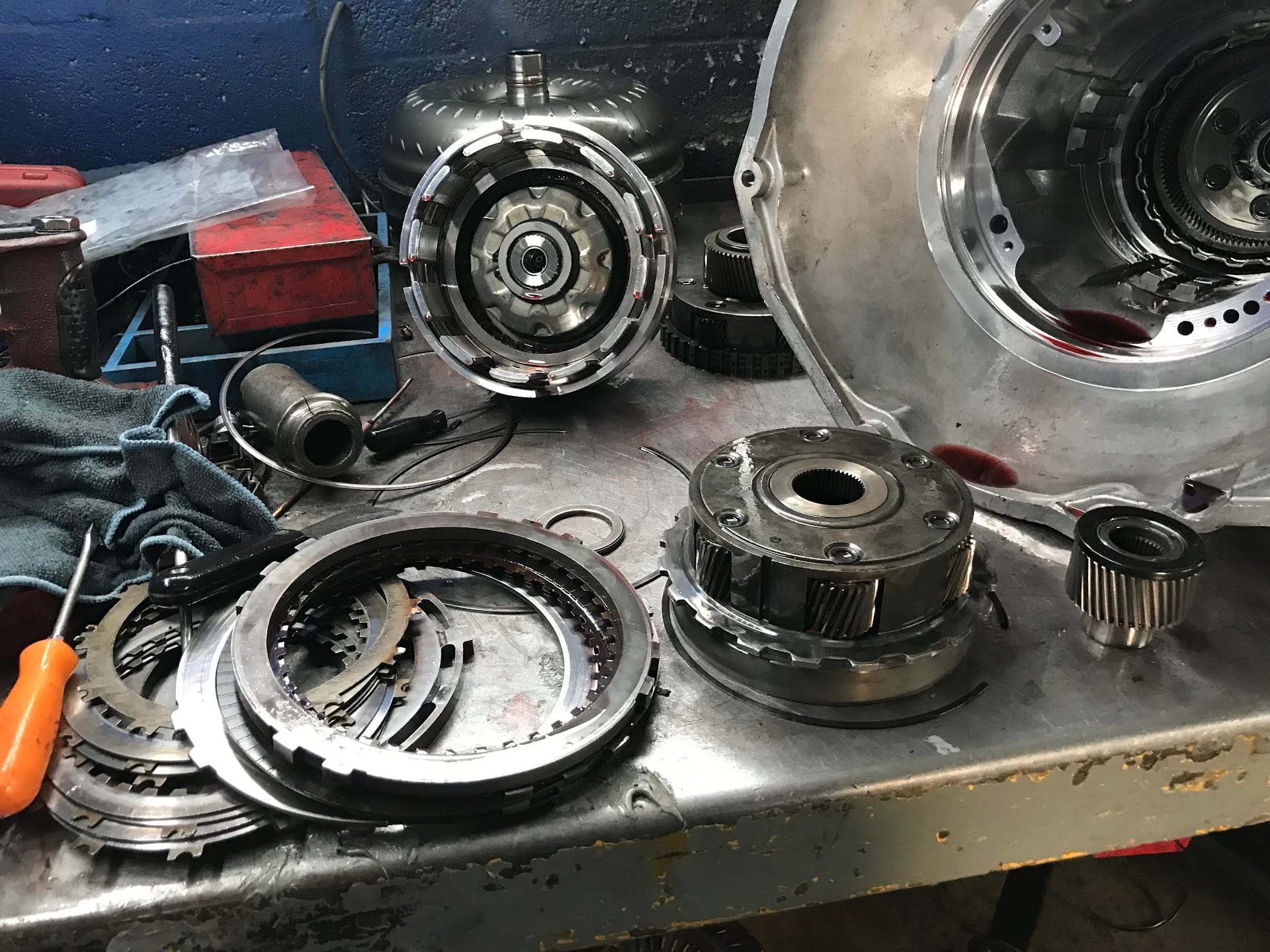 A clutch drum, torque converter and bellhousing laid out on the steel workbench at American International Transmission in Cutler Bay
